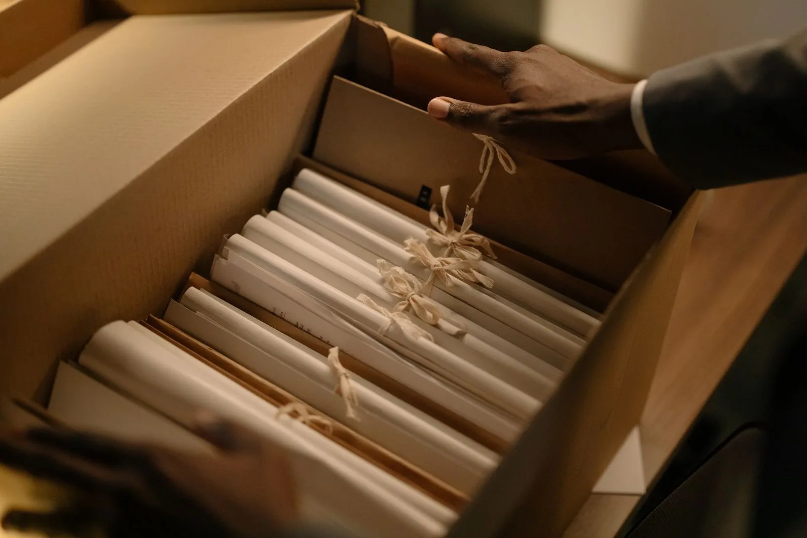 Manos abriendo una caja con expedientes atados con balduque